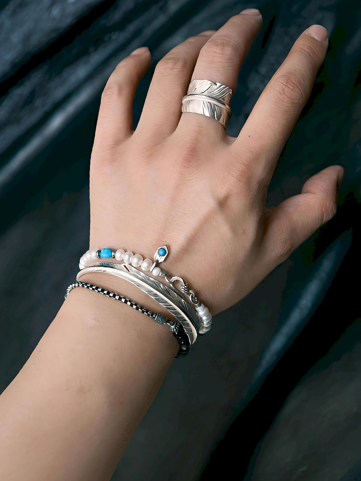 Pearl Rebel worn in a wrist stack with silver bangles and a fine dark bracelet