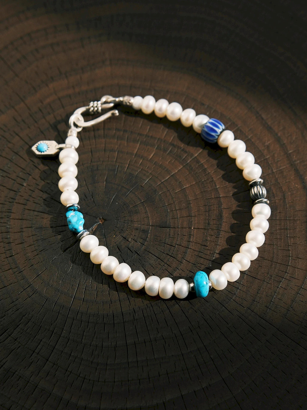 Pearl Rebel arranged on dark wood, with its blue striped bead and turquoise accents spaced around the pearls
