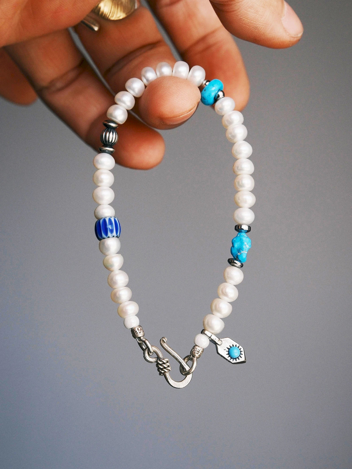 Pearl Rebel held from the top, showing the silver fishhook clasp, white pearls and blue accents