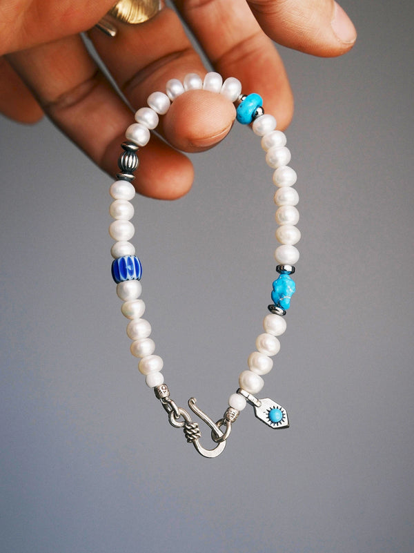 Pearl Rebel held from the top, showing the silver fishhook clasp, white pearls and blue accents