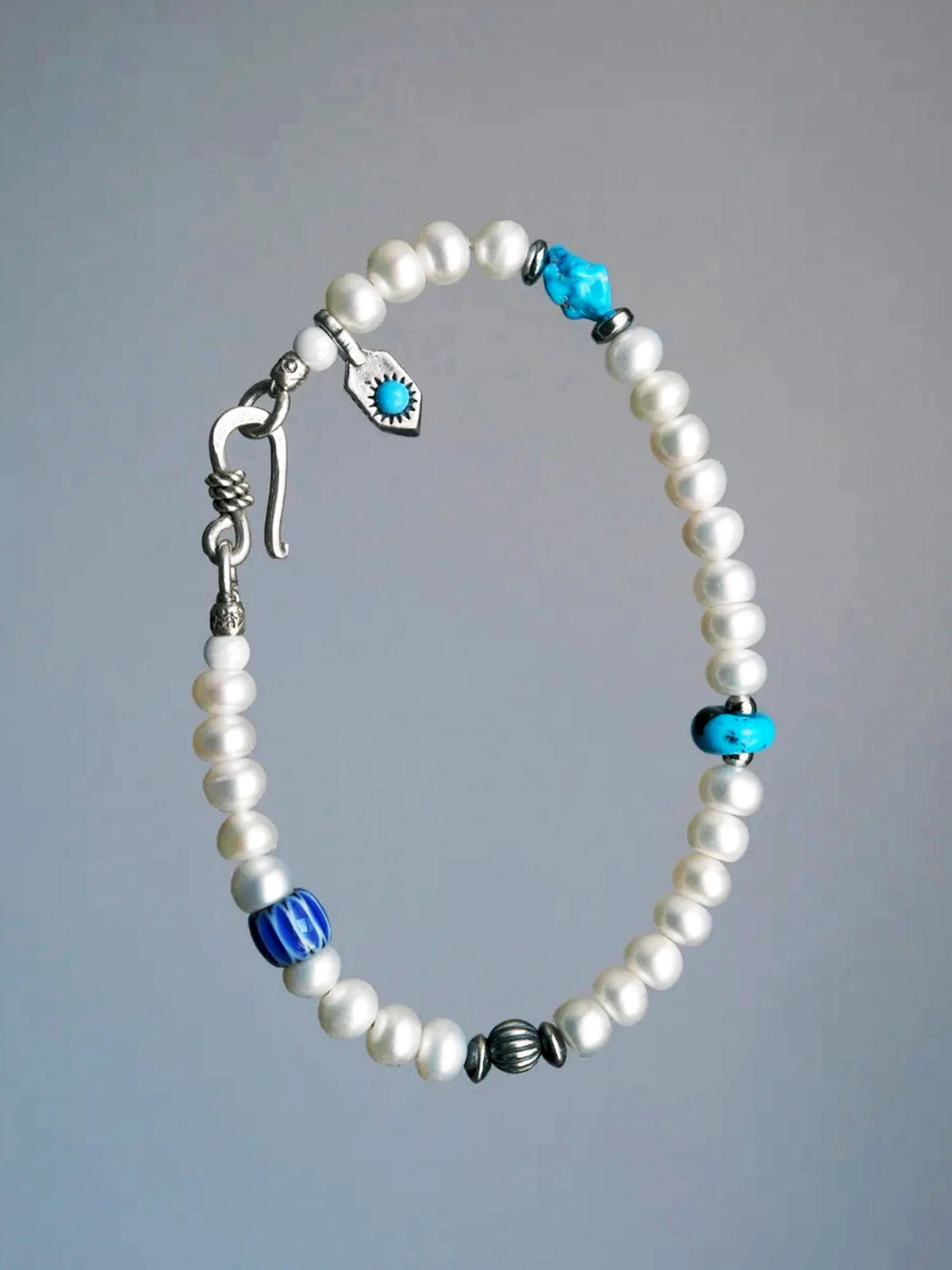 Full view of Pearl Rebel against gray, with white pearls, turquoise and a silver hook clasp