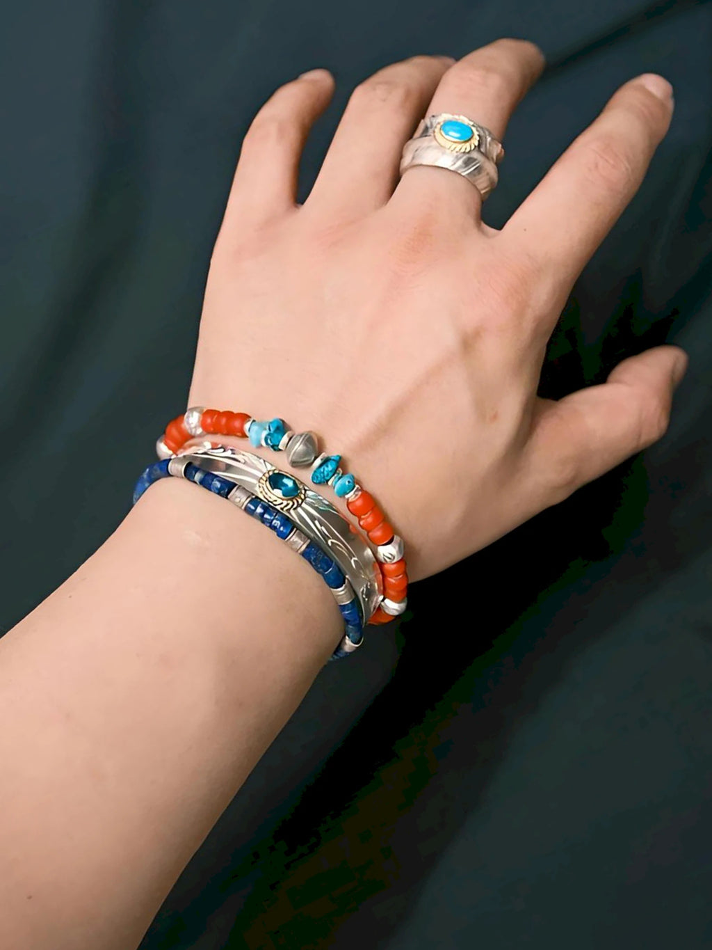 Scarlet Maverick wrist styling with red colored-glaze beads, turquoise accents and an engraved silver centerpiece beside two other bracelets.