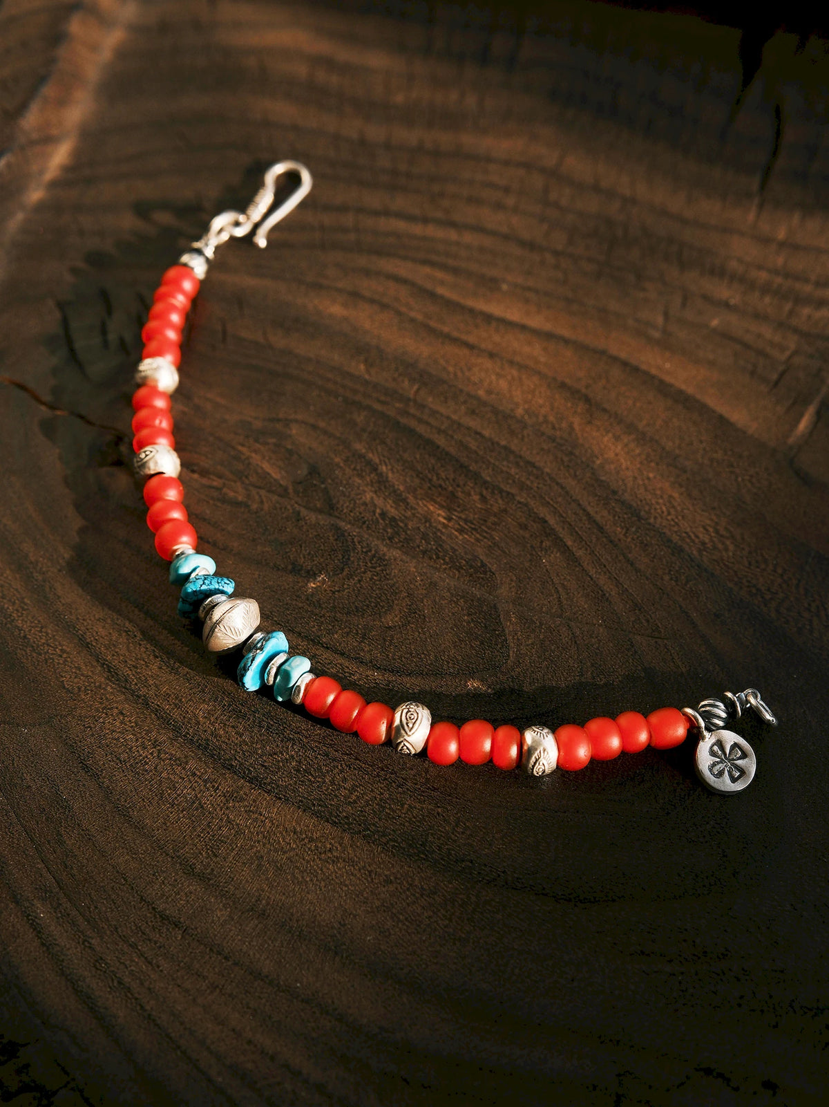 Open Scarlet Maverick bracelet on dark wood, with red colored-glaze beads, turquoise accents, engraved silver details and a round charm.