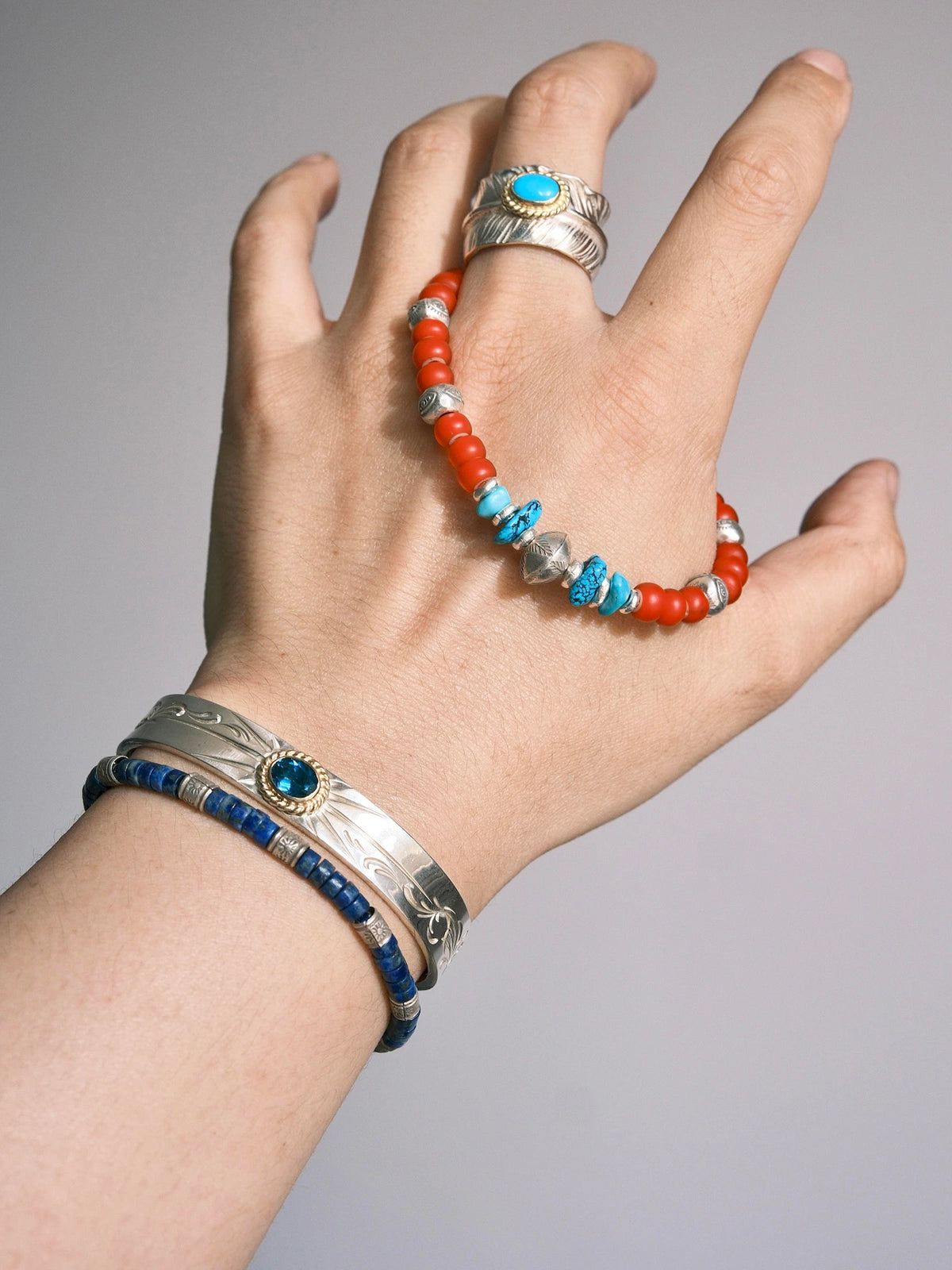 Scarlet Maverick draped across a hand, showing turquoise accents around an engraved silver bead and rows of red colored-glaze beads.