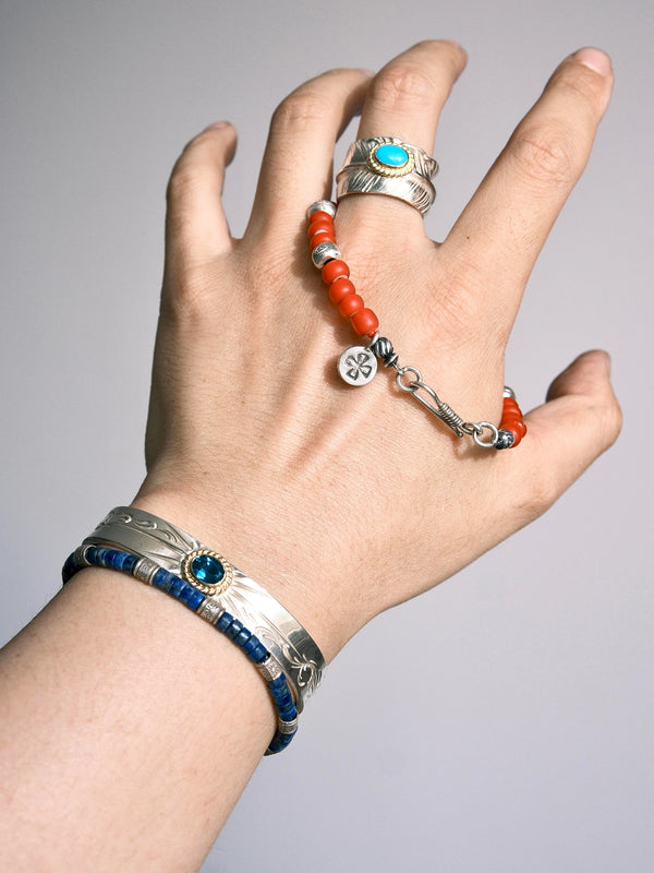 Close view of Scarlet Maverick draped over a hand, highlighting its fishhook clasp, round stamped charm and red colored-glaze beads.