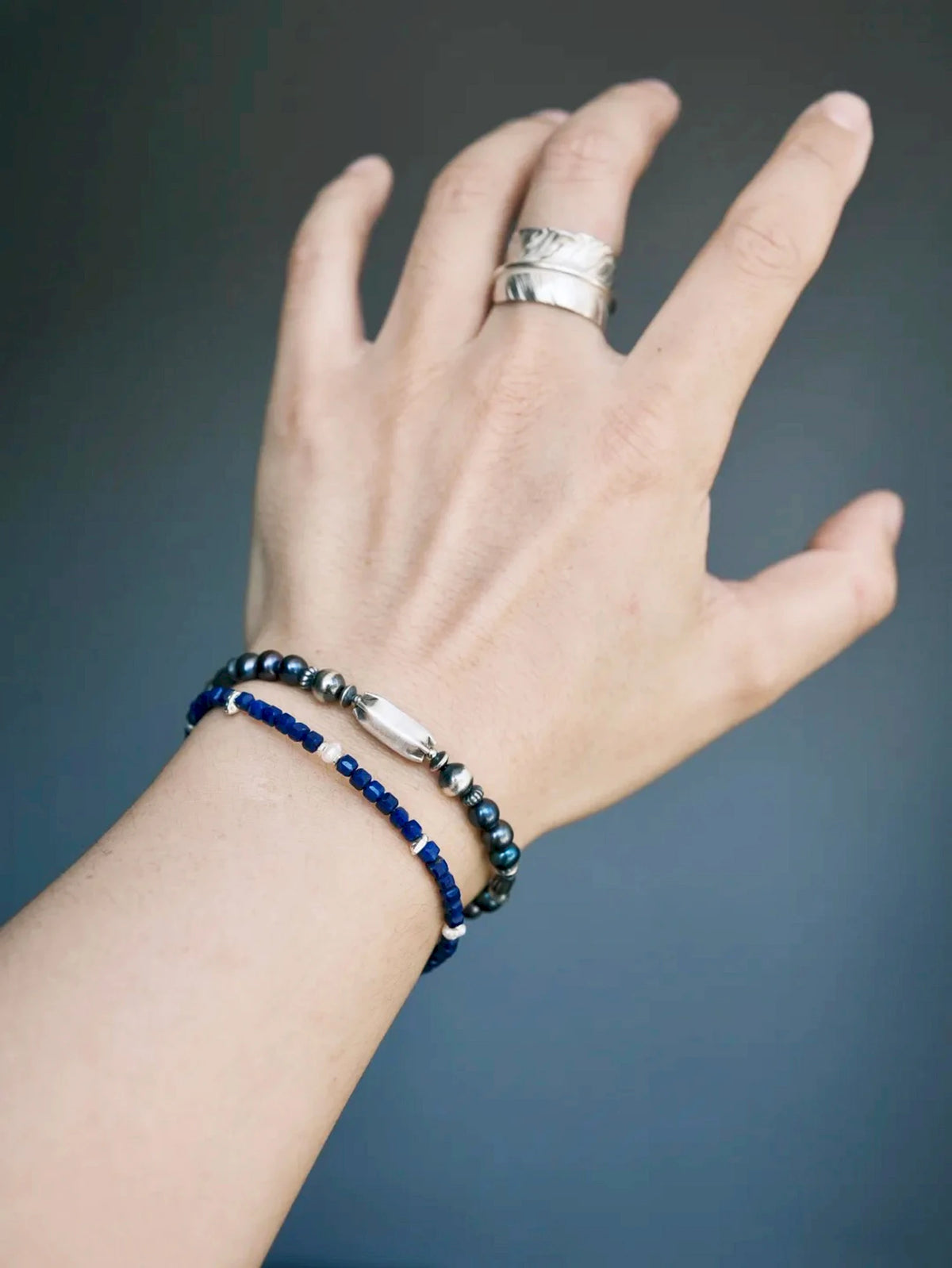 Midnight Envoy on a wrist beside a slim blue-bead bracelet, highlighting its elongated silver centerpiece and dark pearls.