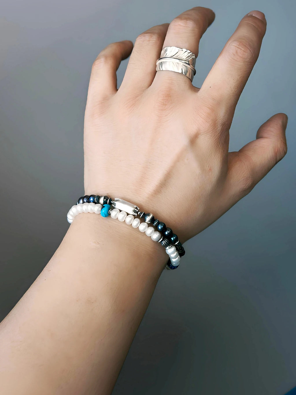 Midnight Envoy dark pearl bracelet stacked with a separate white-bead bracelet and turquoise-colored accent, with a silver-tone ring above.