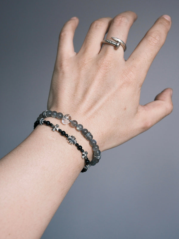 Grey Sovereign labradorite and clear quartz bracelet on a wrist, styled beside a separate black-bead bracelet with silver-tone floral details.