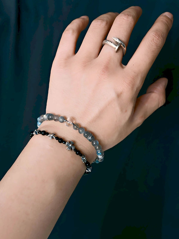 Grey Sovereign labradorite and clear quartz bracelet worn with a separate black-bead bracelet, against a dark blue textured background.