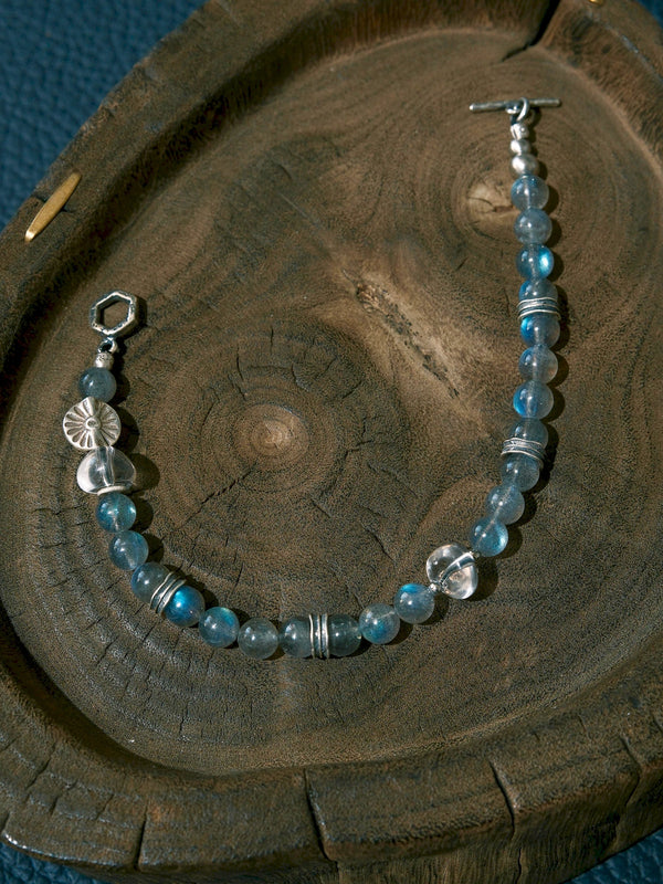 Open Grey Sovereign bracelet on a wooden tray, showing labradorite beads, clear quartz accents, a sun-motif bead and both toggle ends.