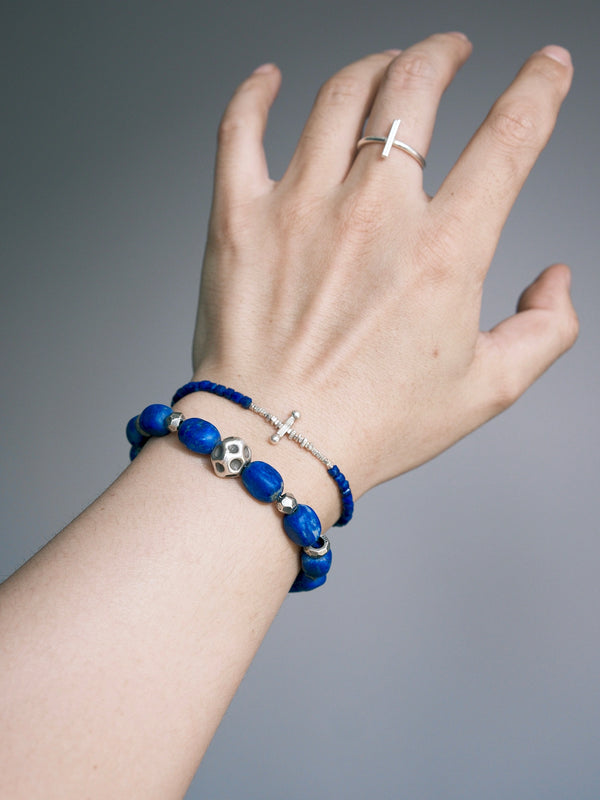 Lapis lazuli and silver bracelet worn beside a thinner blue bracelet, with a silver-colored ring visible.