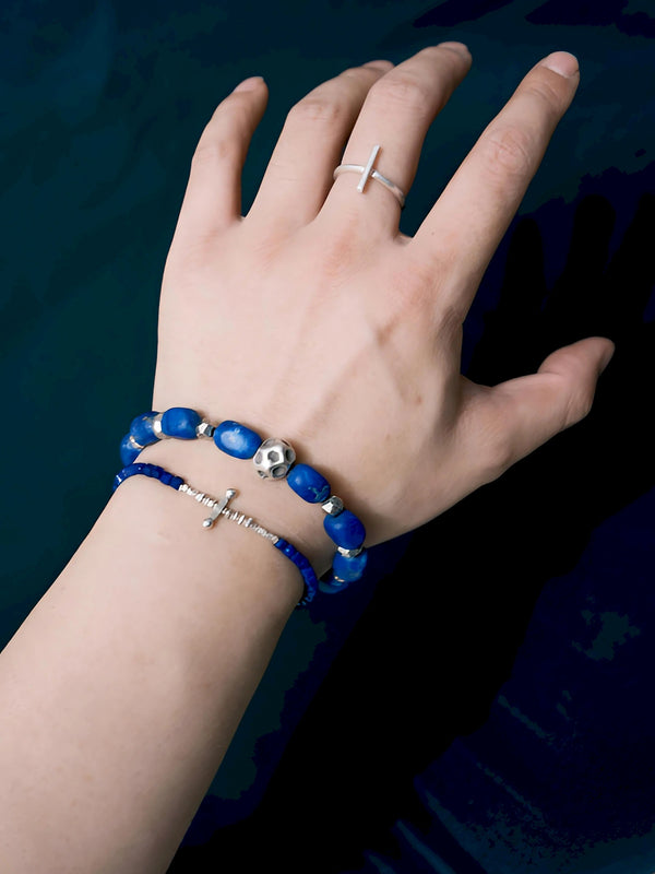 Blue lapis lazuli bracelet with a cratered silver centerpiece, worn with a thinner blue bracelet against a dark background.