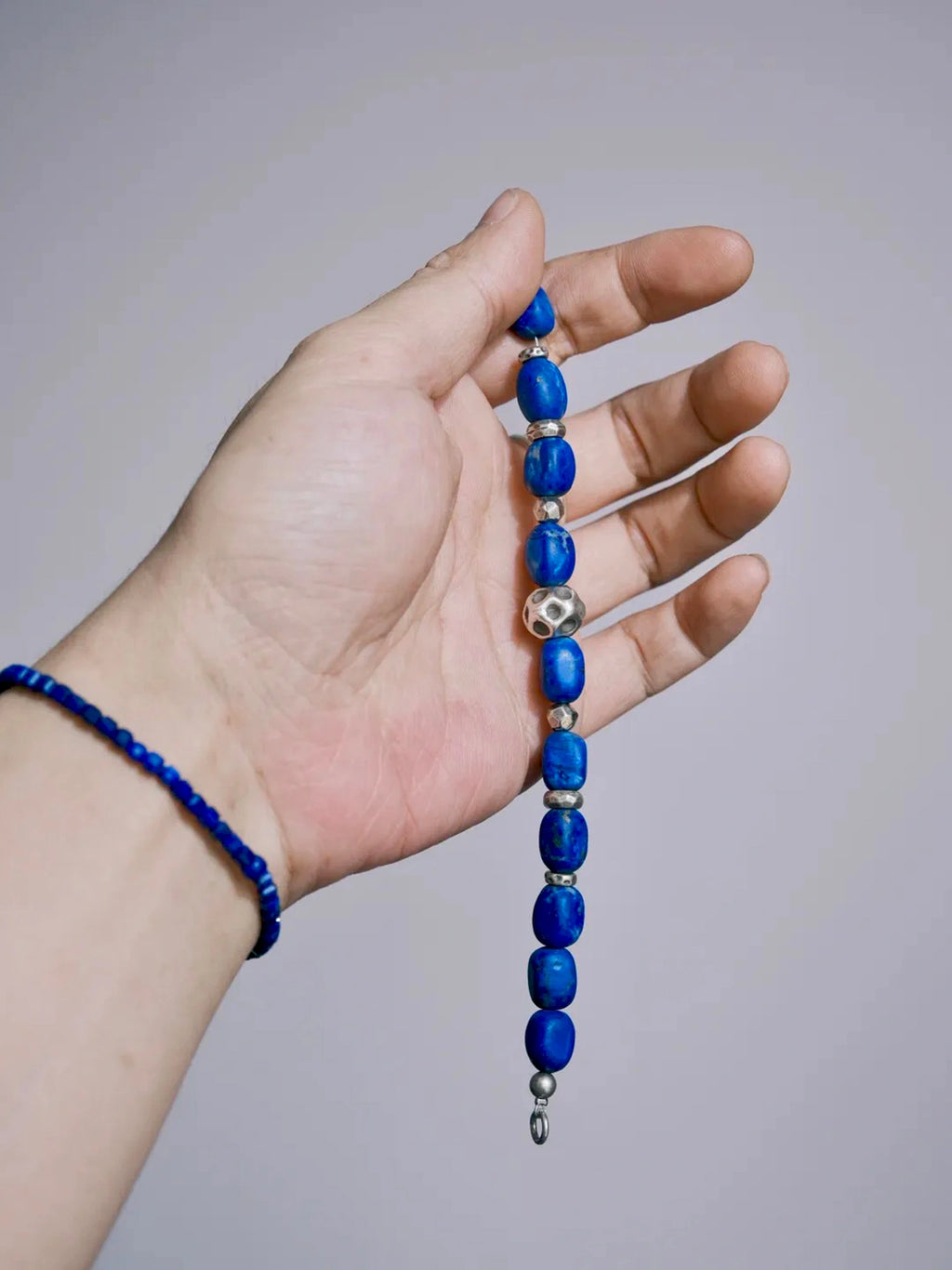 Open lapis lazuli bracelet draped across a palm, showing blue beads, silver details and an end ring.
