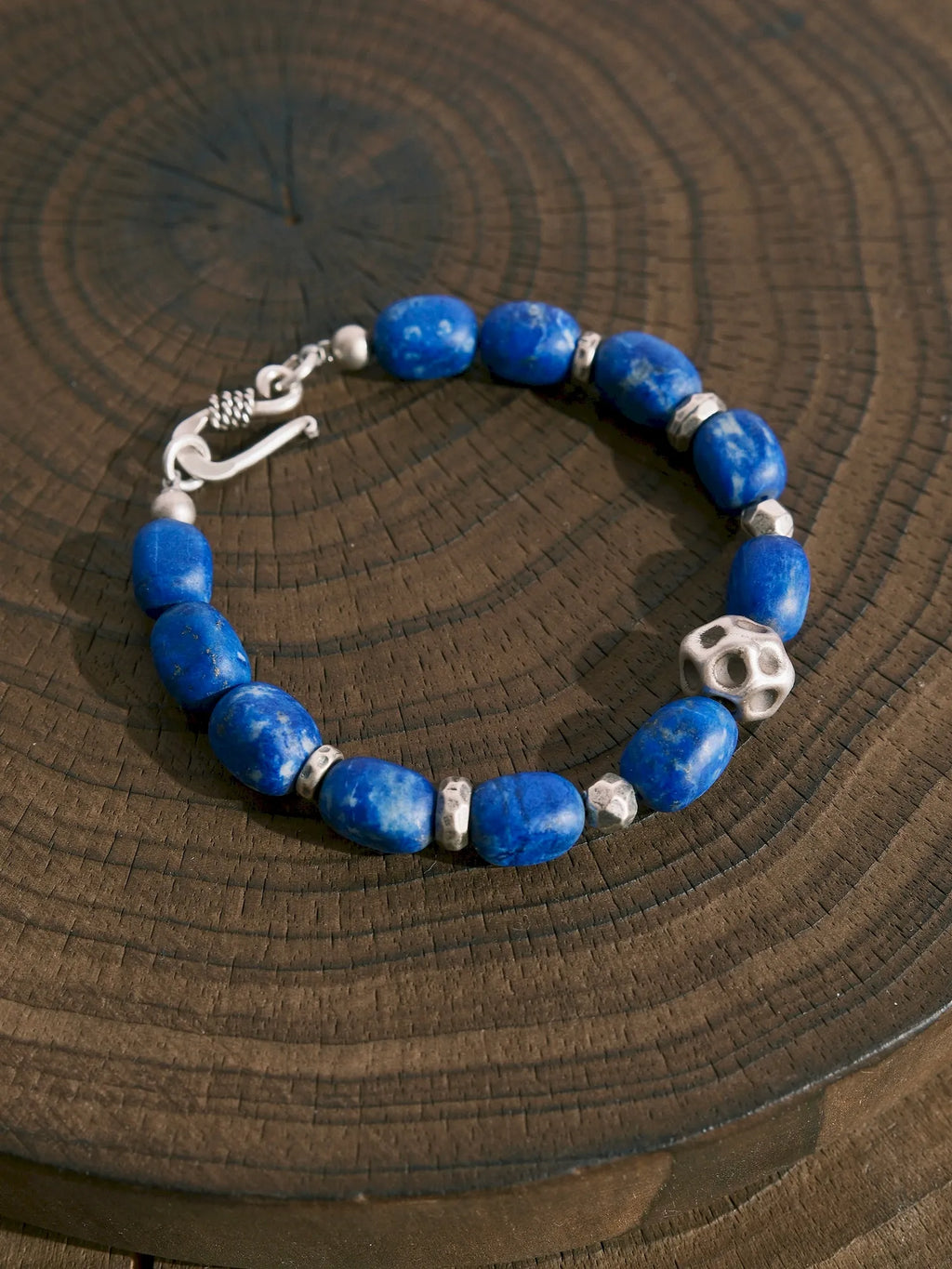 Lapis lazuli and silver bracelet arranged in a loop on a wooden surface, with the hook clasp at the left.