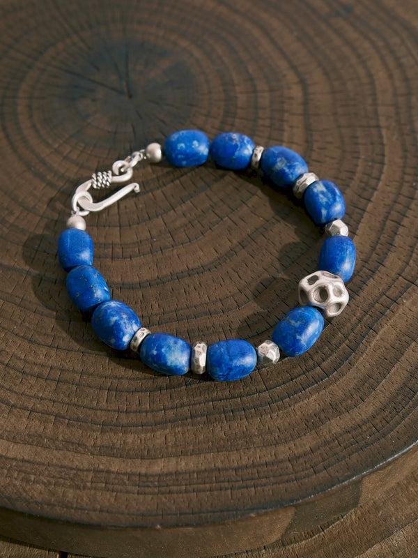 Lapis lazuli and silver bracelet arranged in a loop on a wooden surface, with the hook clasp at the left.