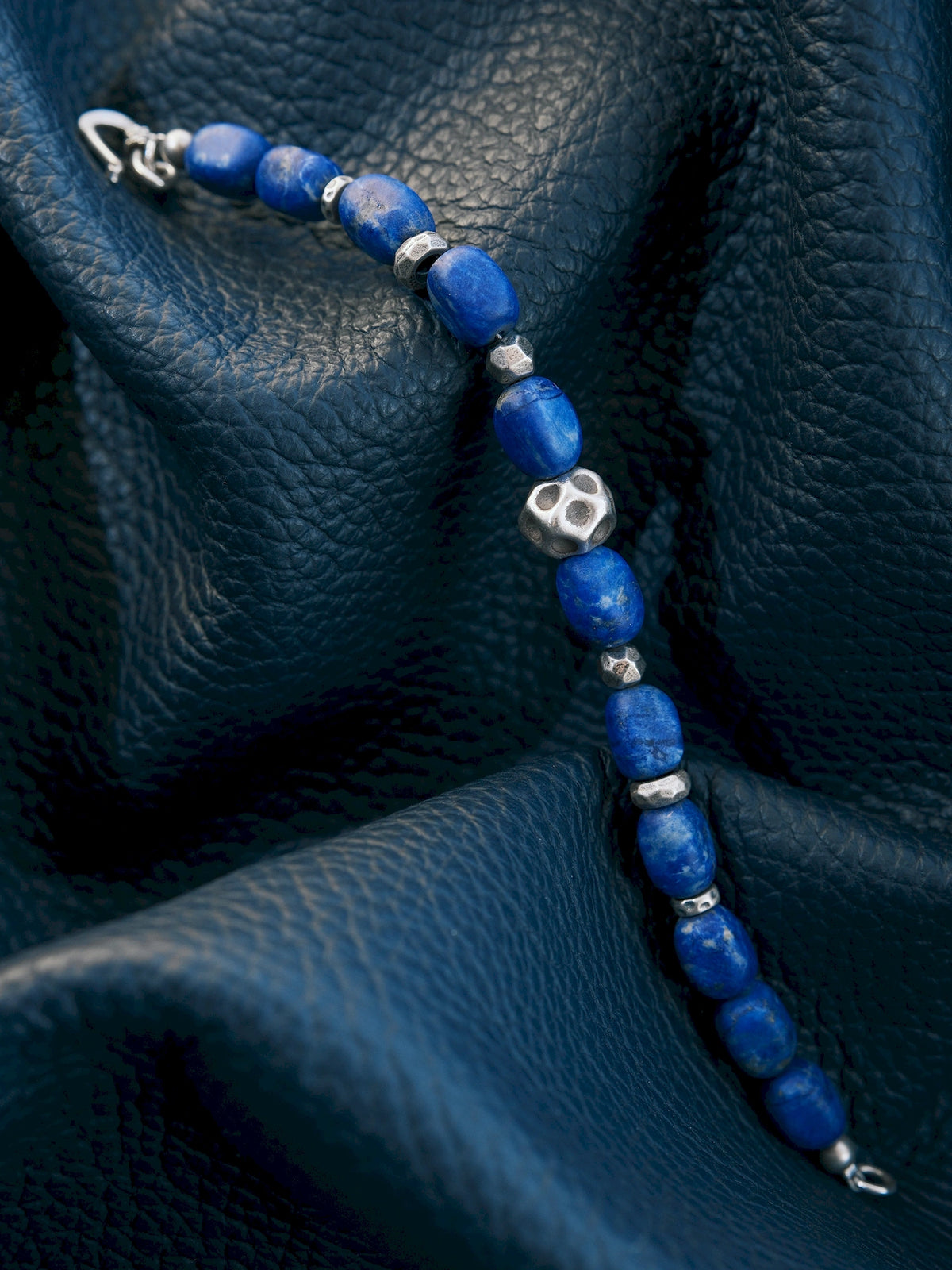 Close-up of blue lapis lazuli beads and a cratered silver centerpiece across a dark blue textured surface.