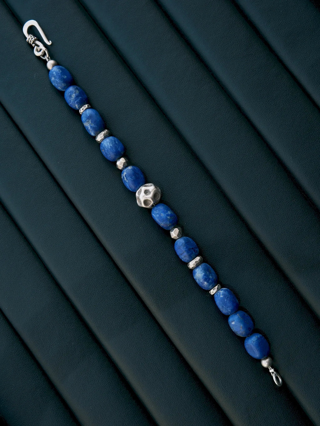 Unfastened lapis lazuli and silver bracelet laid diagonally on a dark padded surface, showing both clasp ends.
