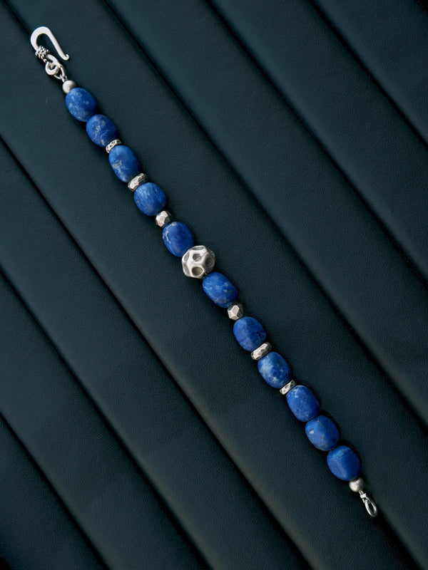 Unfastened lapis lazuli and silver bracelet laid diagonally on a dark padded surface, showing both clasp ends.