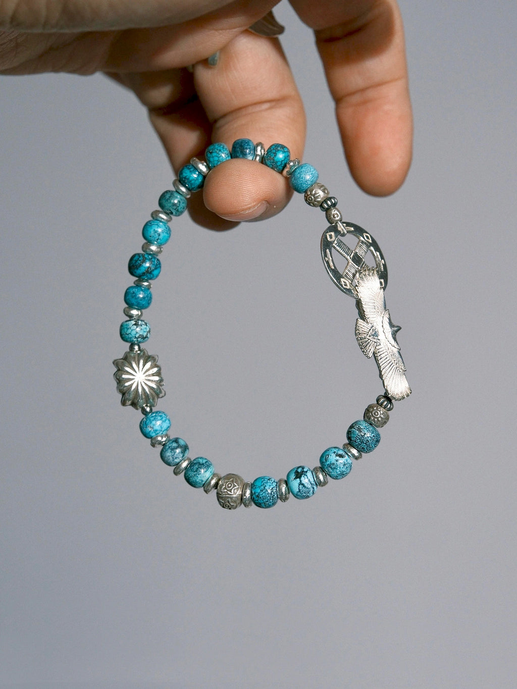 Sun Seeker turquoise and silver bracelet held between fingers, showing the eagle clasp and flower-shaped accent.