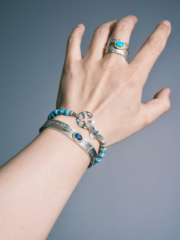 Sun Seeker turquoise bracelet worn with its flower-shaped silver accent facing up, beside a cuff and ring.