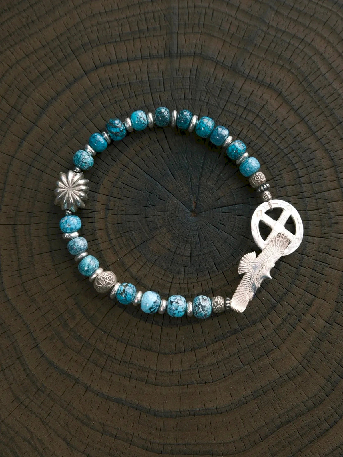 Sun Seeker turquoise and silver eagle bracelet arranged in a circle on wood, showing its clasp and flower-shaped accent.