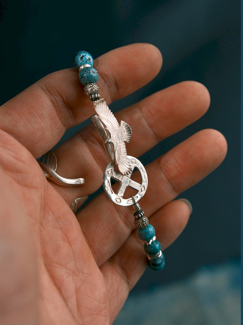 Sun Seeker bracelet worn against dark clothing, with the eagle clasp visible below a cuff and a ring on the hand.