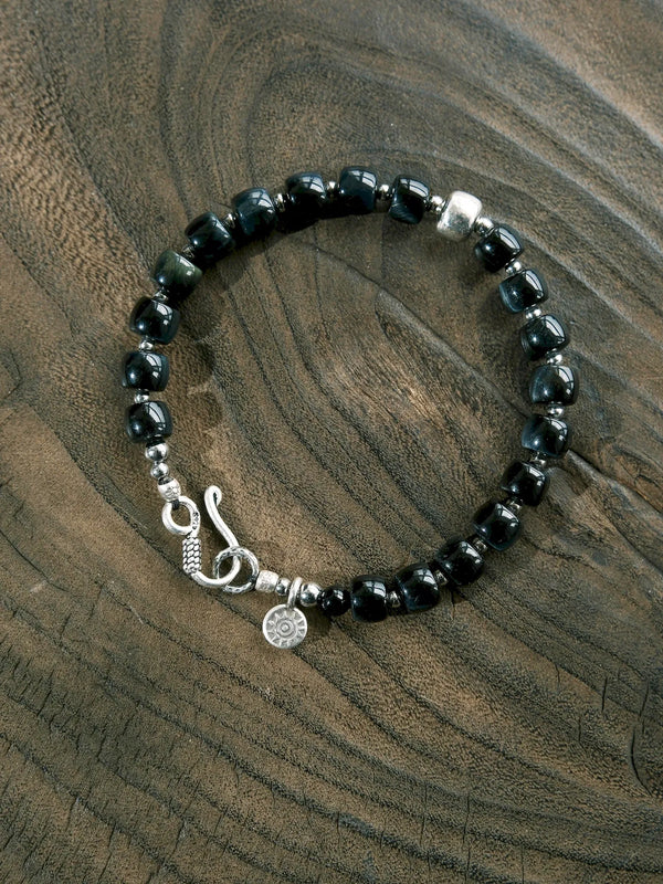 Blue Strategist dark blue beaded bracelet arranged in a circle on wood, with a silver-tone accent and hook clasp.