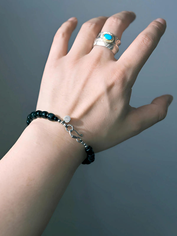 Blue Strategist dark blue beaded bracelet worn alone, showing the hook clasp and round sun-patterned detail.