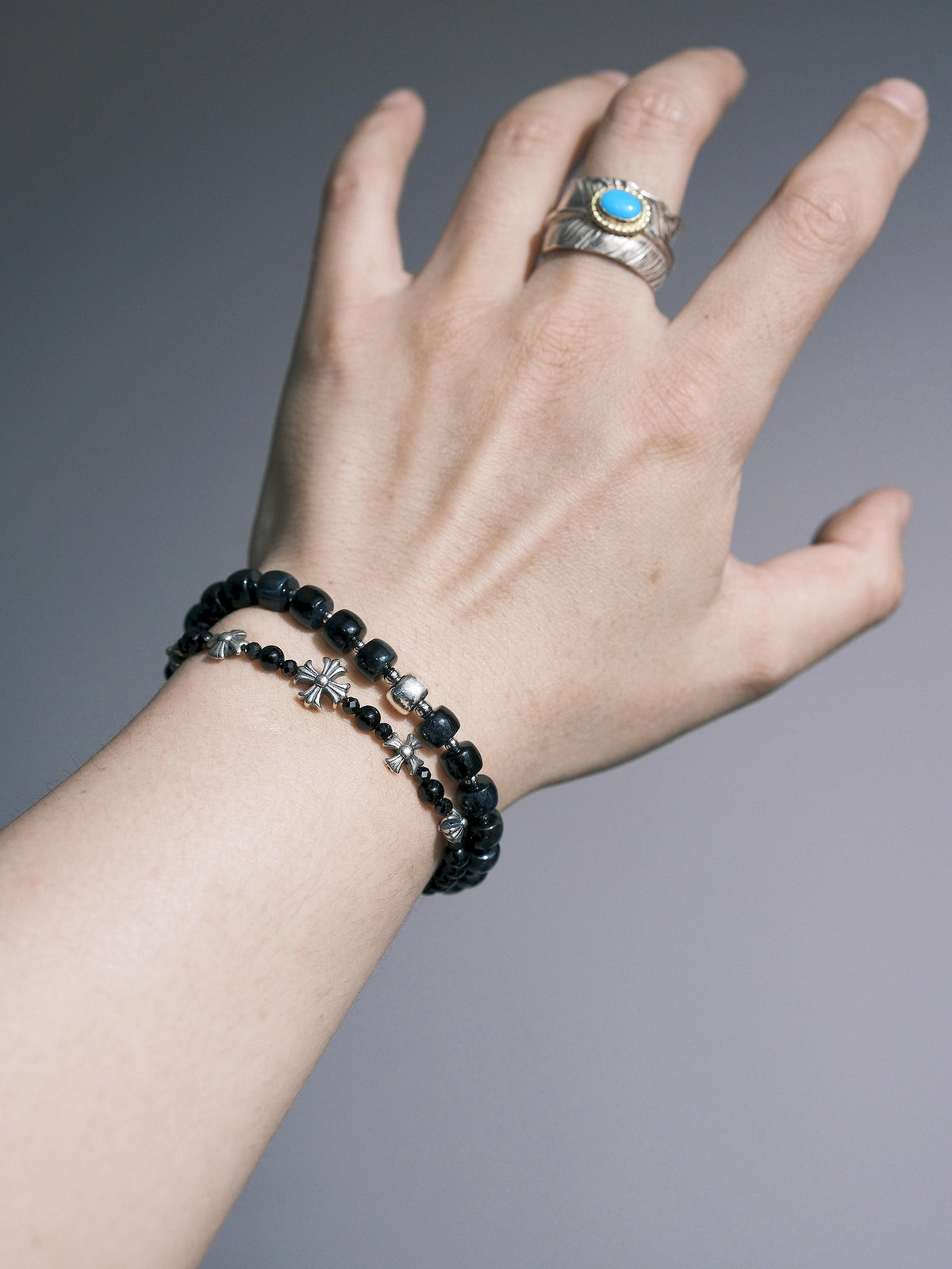Blue Strategist bracelet stacked with a thinner black beaded bracelet with cross-shaped metal details.