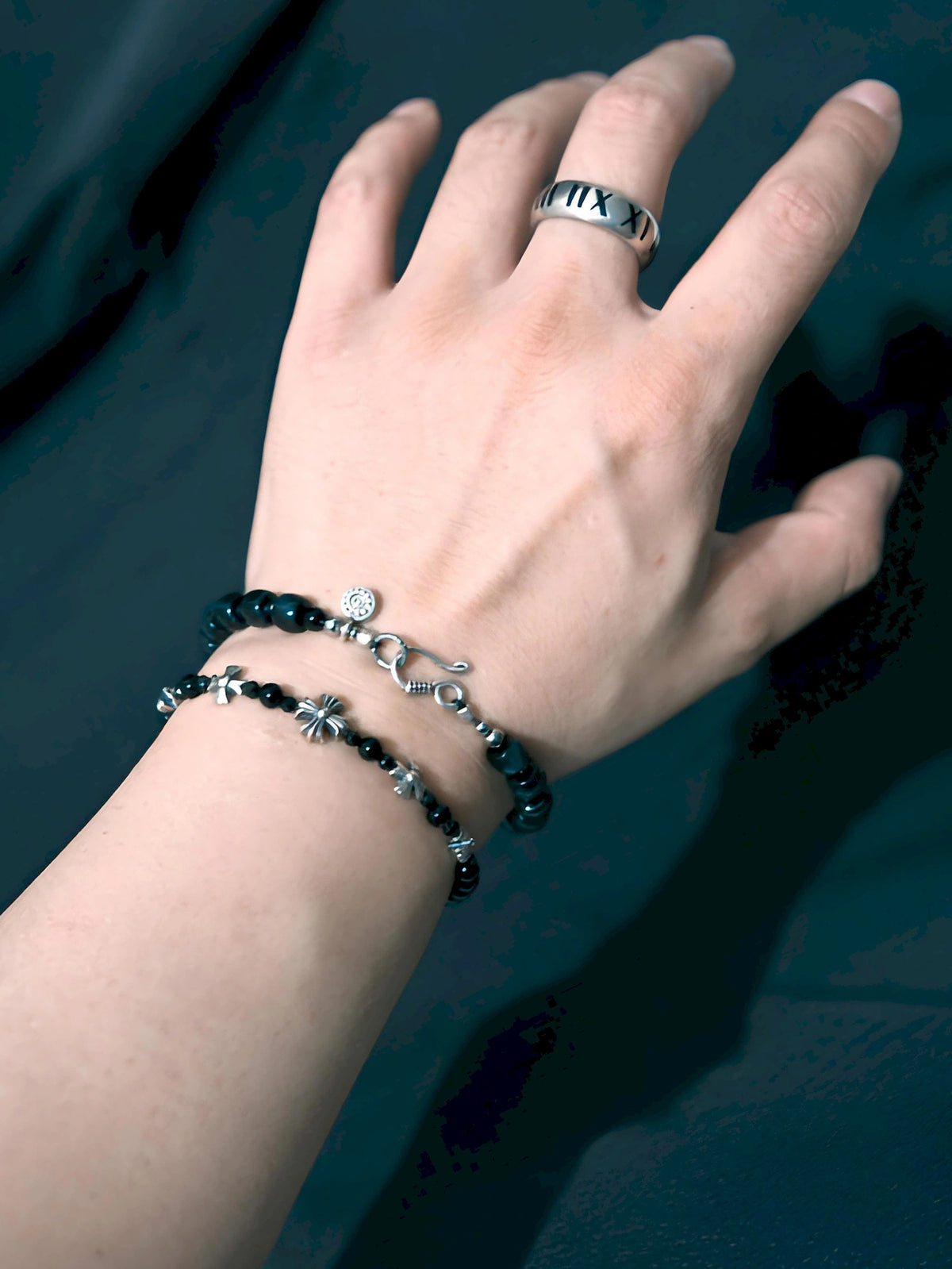 Blue Strategist bracelet showing its hook clasp and sun-patterned detail in a wrist stack against a dark background.