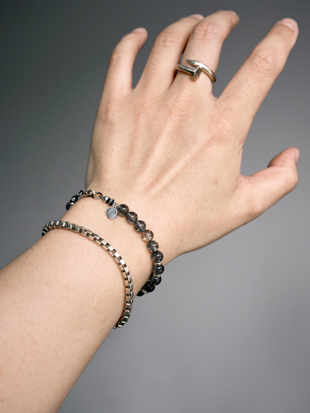 Shadow Sentinel bracelet stacked with a chain bracelet, showing the fishhook clasp and leaf-shaped detail.