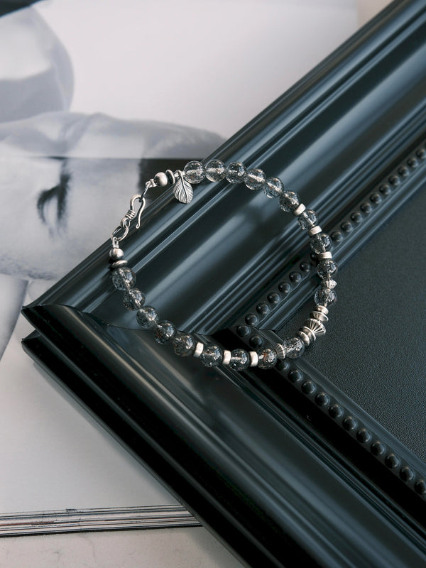 Shadow Sentinel bracelet arranged over a diagonal black picture frame, showing the clasp and beaded strand.