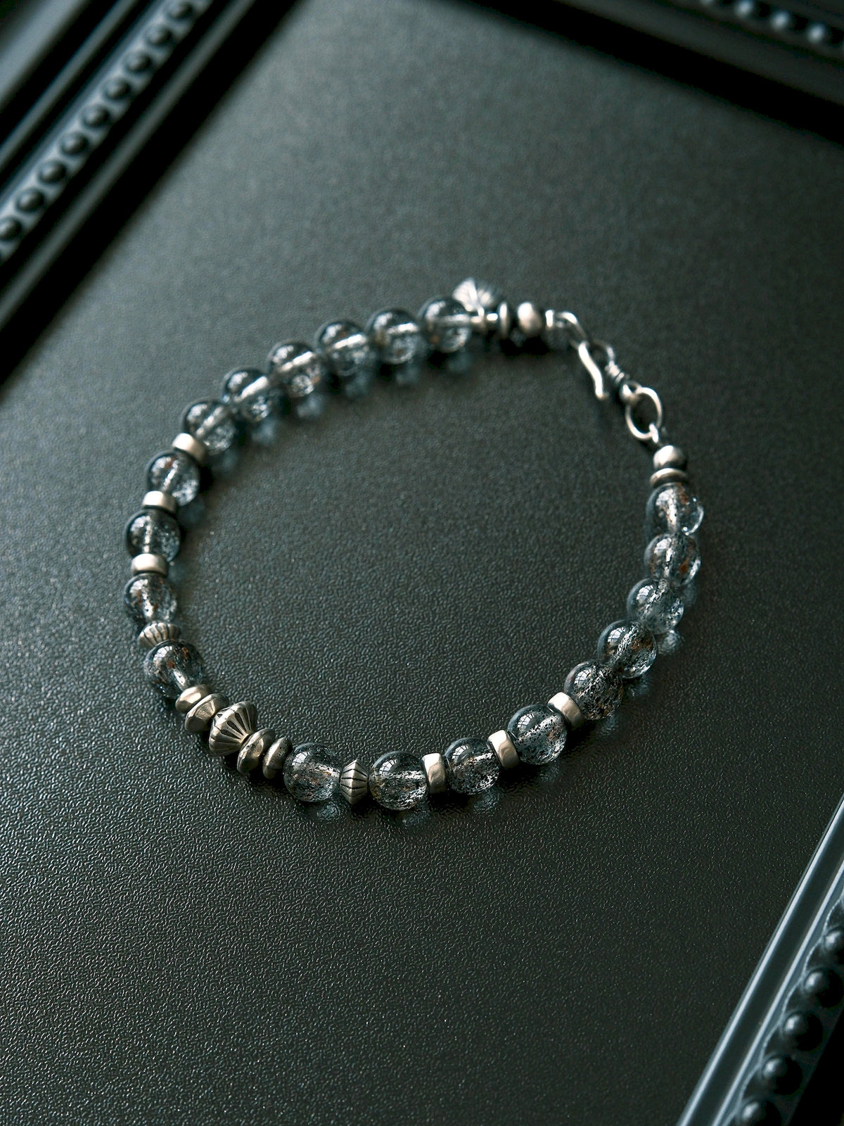 Shadow Sentinel bracelet on a textured black surface, showing dark translucent beads and geometric metal accents.