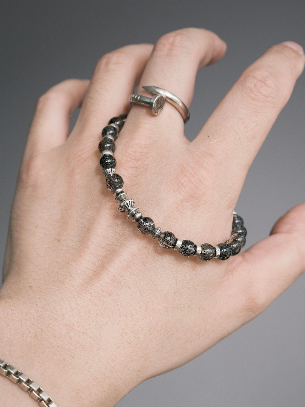 Shadow Sentinel bracelet held in hand, showing translucent dark beads, a fishhook clasp and a leaf-shaped detail.