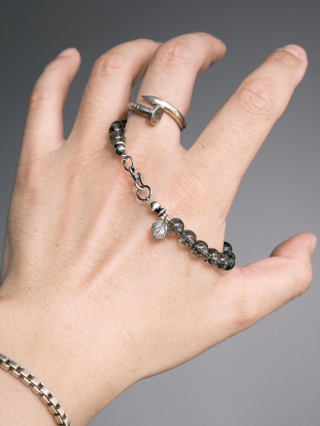 Shadow Sentinel bracelet held in hand, showing translucent dark beads, a fishhook clasp and a leaf-shaped detail.