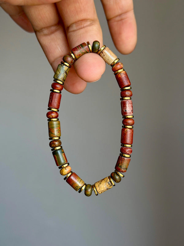 Earth Nomad Picasso jasper bracelet with gold-tone hematite spacers held against a gray background.