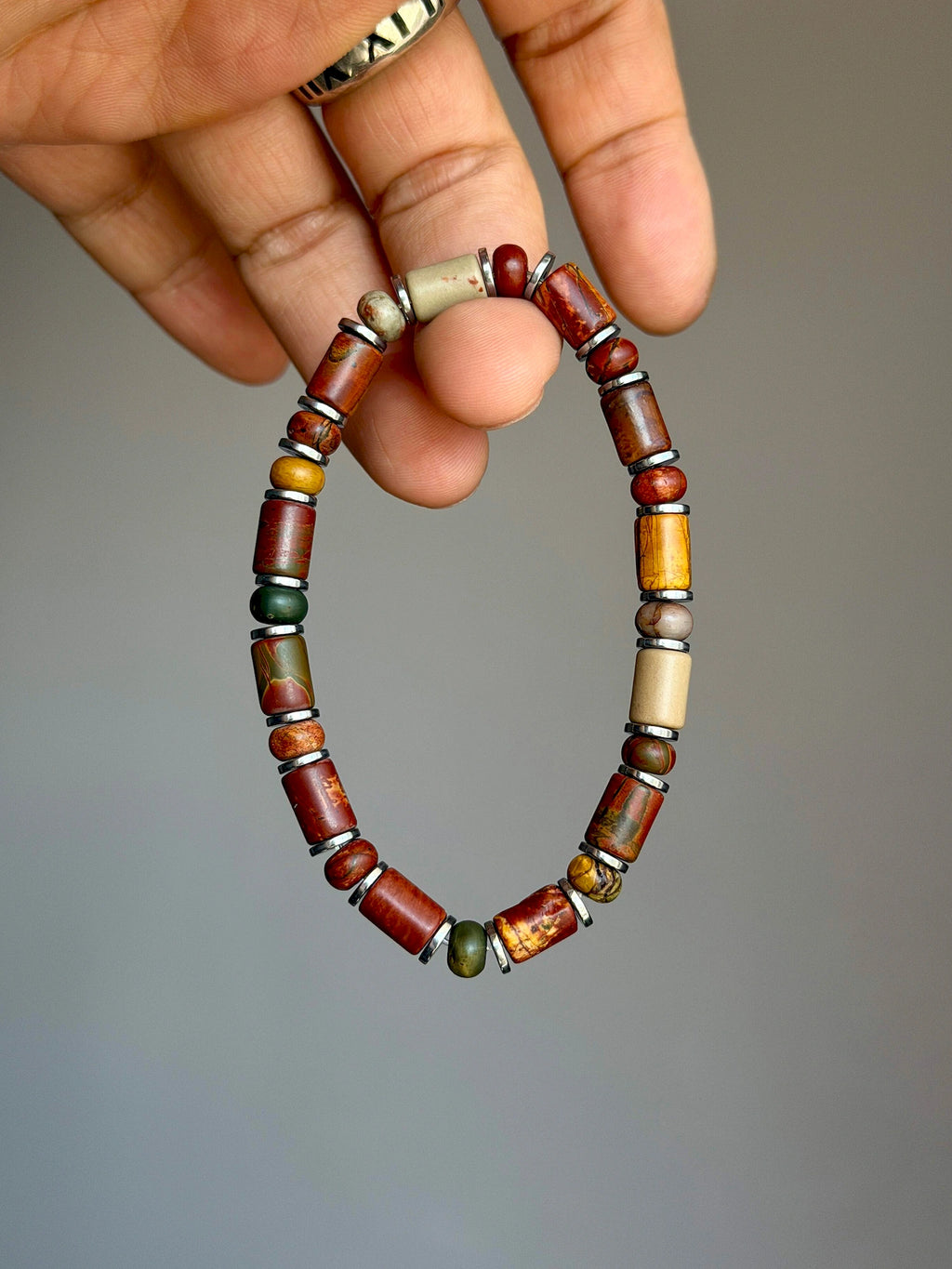 Earth Nomad Picasso jasper bracelet with silver-tone hematite spacers held between fingers.