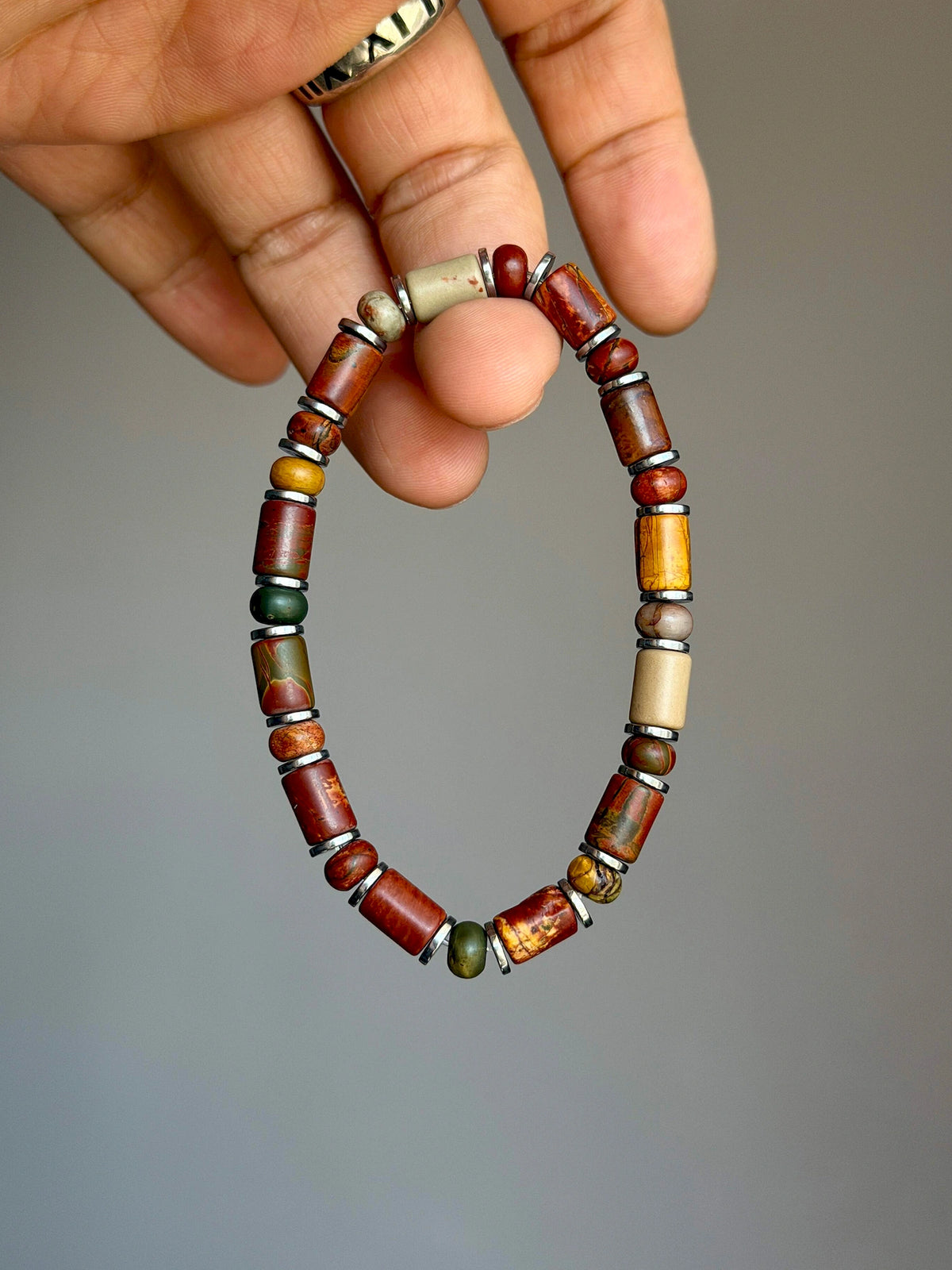 Earth Nomad Picasso jasper bracelet with silver-tone hematite spacers held between fingers.