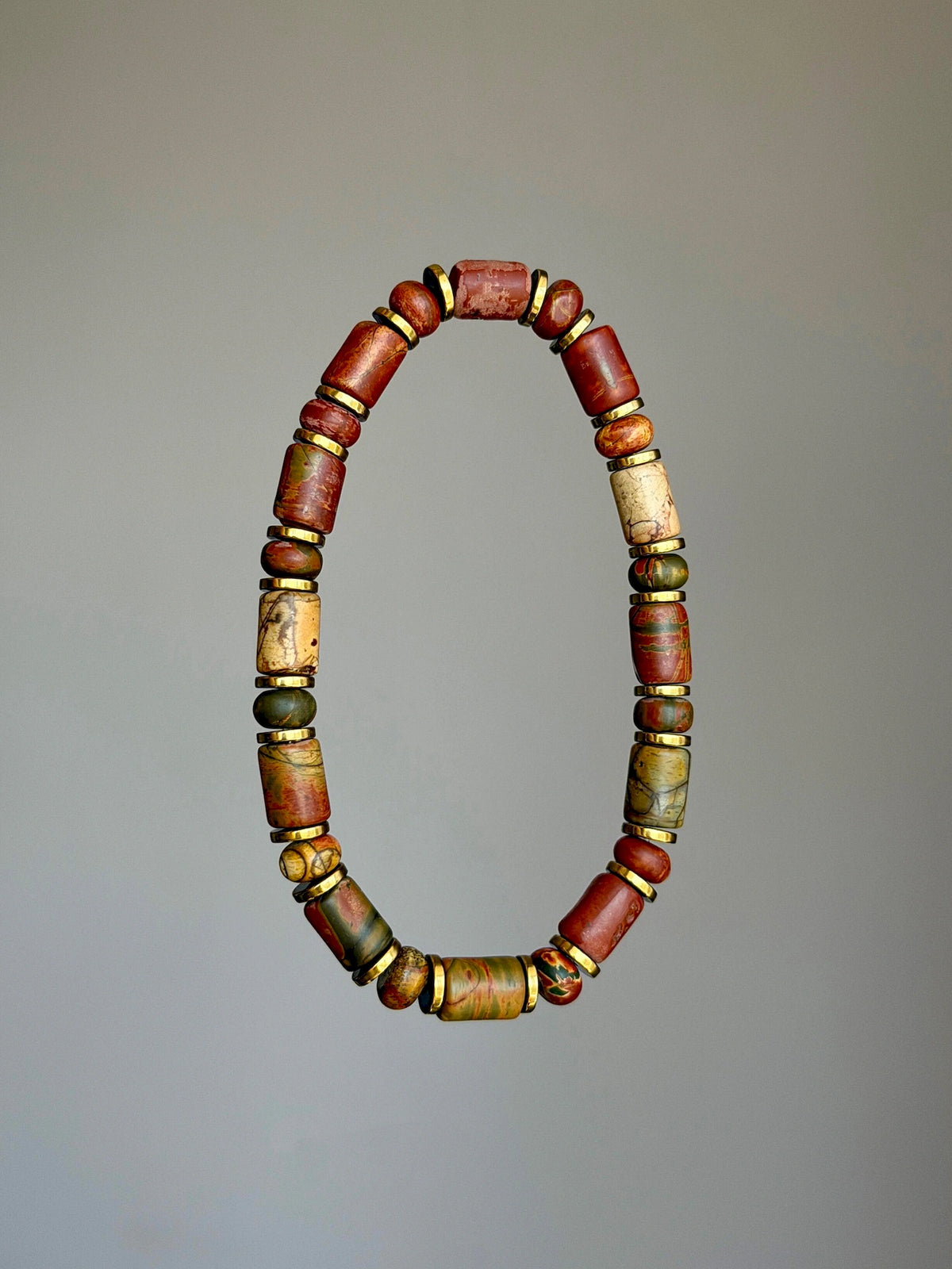 Gold-tone Earth Nomad Picasso jasper bracelet shown alone in an oval against a gray background.