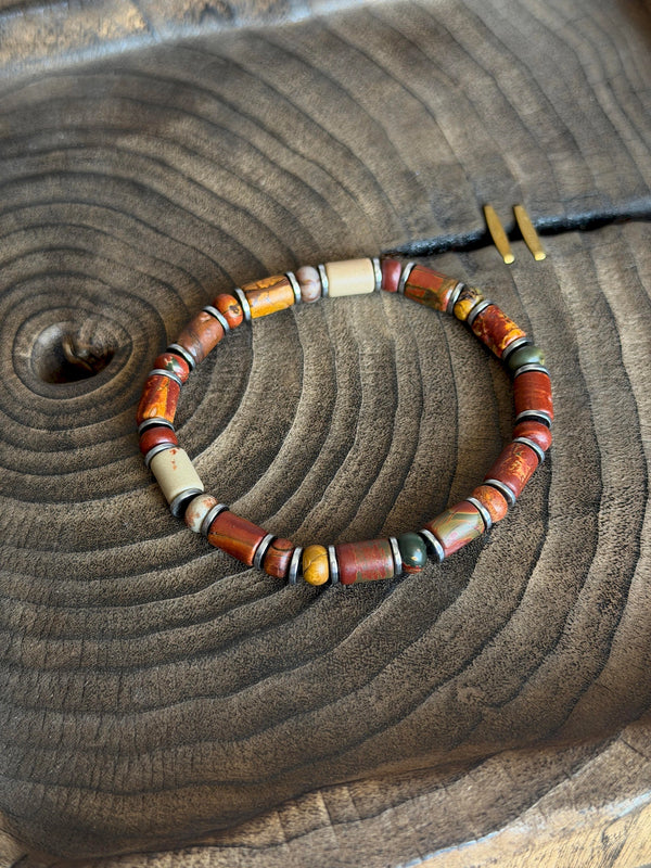 Silver-tone Earth Nomad Picasso jasper bracelet resting on a circular wood-grain surface.