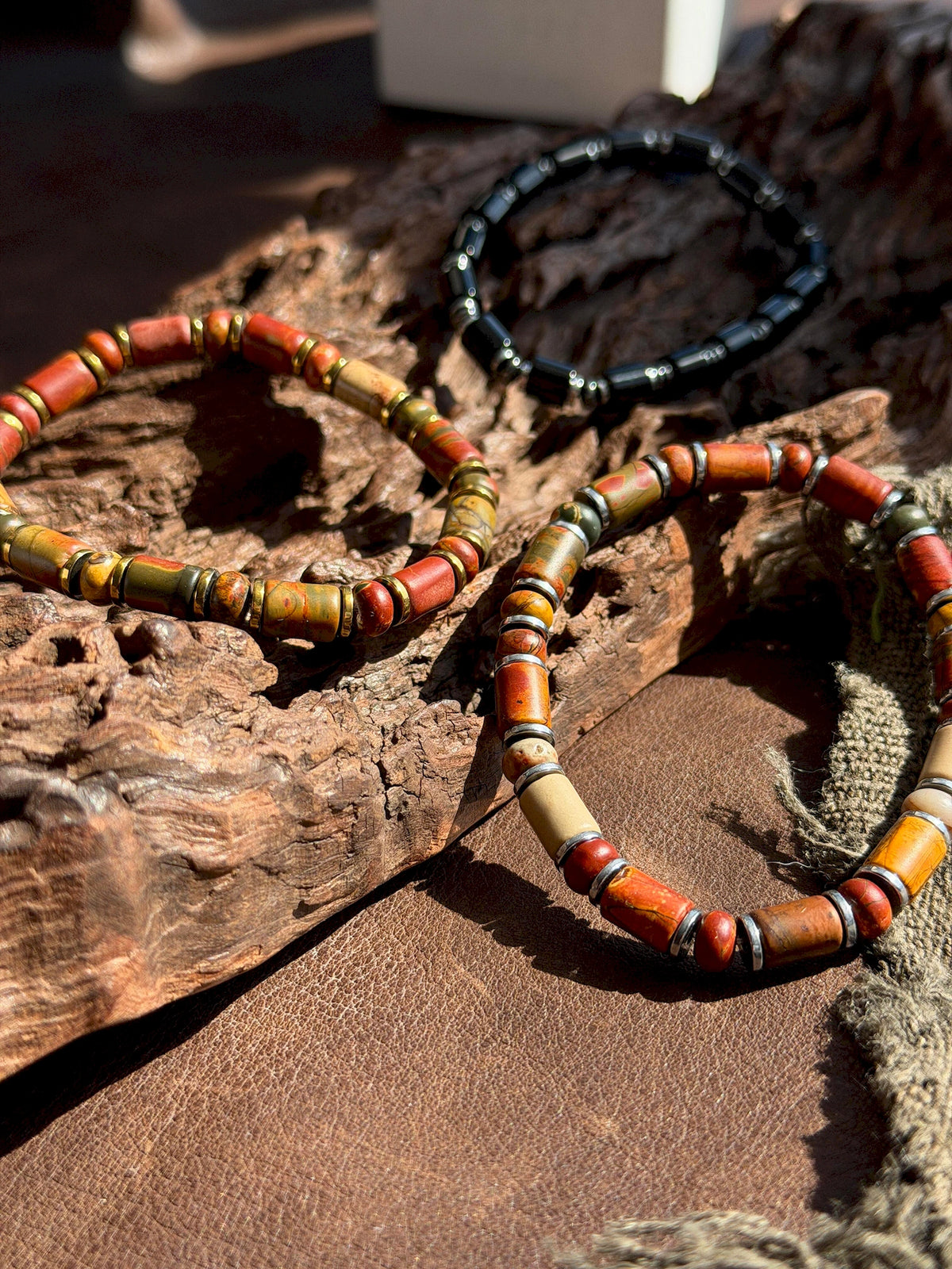 Gold-tone and silver-tone Earth Nomad bracelets arranged on bark and brown leather beside a dark bracelet.
