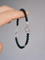 Silver Ego black onyx bracelet held against a gray background, showing the silver male symbol and fishhook clasp.