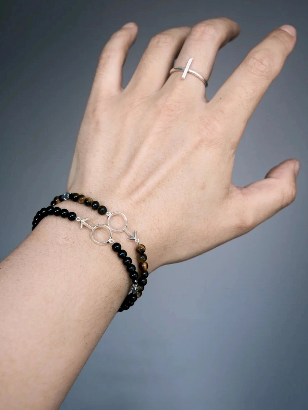 Silver Ego black onyx male-symbol bracelet worn beside a brown beaded bracelet, with a silver-tone bar ring.