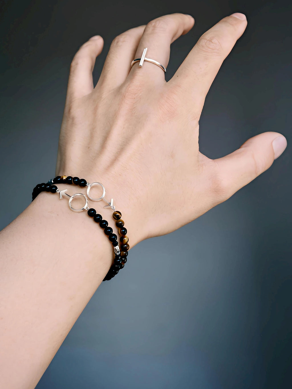 Two male-symbol bracelets on the wrist, including the black onyx Silver Ego, with a silver-tone bar ring.