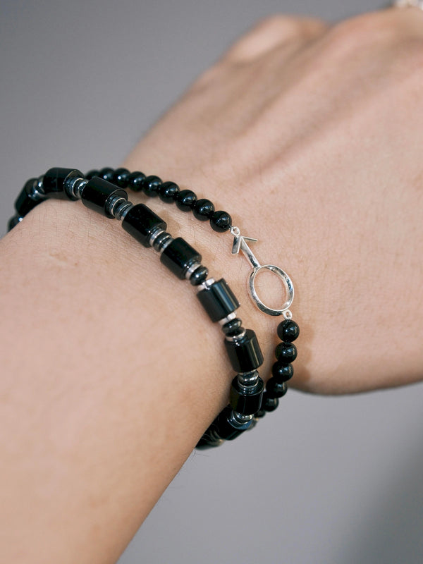 Close-up of Silver Ego black onyx beads and silver male symbol on the wrist beside a cylindrical-bead bracelet.