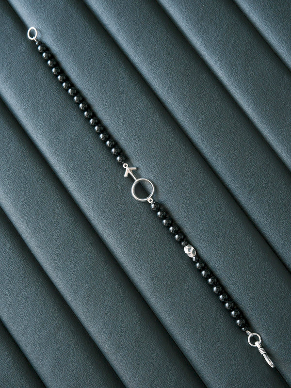 Silver Ego bracelet laid open diagonally on a dark ribbed surface, showing the bead strand and fishhook closure.