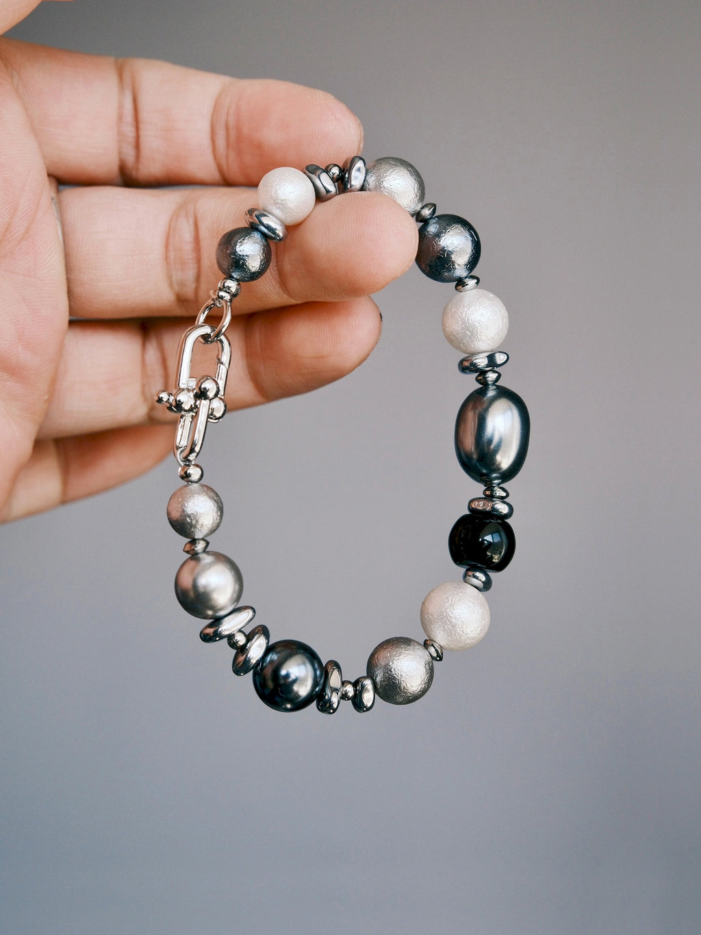 Quiet Rebel shell beads and silver-tone hematite bracelet held between fingers, with the horseshoe clasp visible.