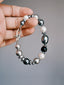 Quiet Rebel shell beads and silver-tone hematite bracelet held between fingers, with the horseshoe clasp visible.