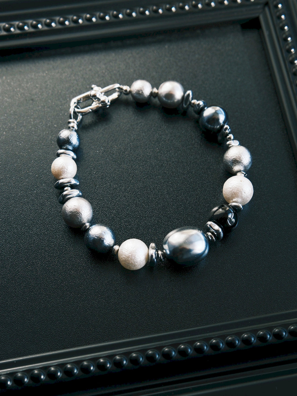 Quiet Rebel men's bracelet in a closed circle on a black tray, showing round and oval beads with silver-tone spacers.