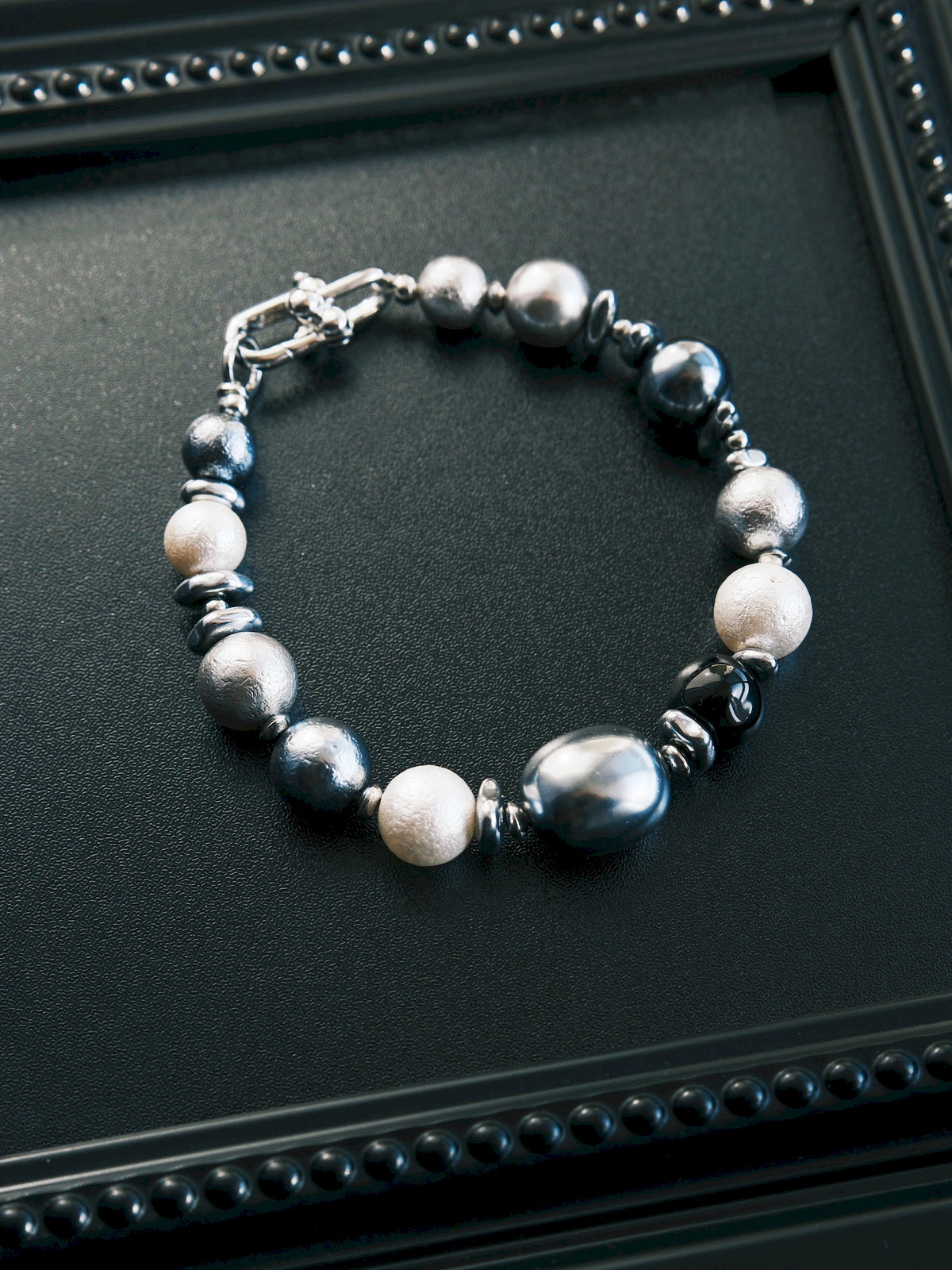 Quiet Rebel men's bracelet in a closed circle on a black tray, showing round and oval beads with silver-tone spacers.